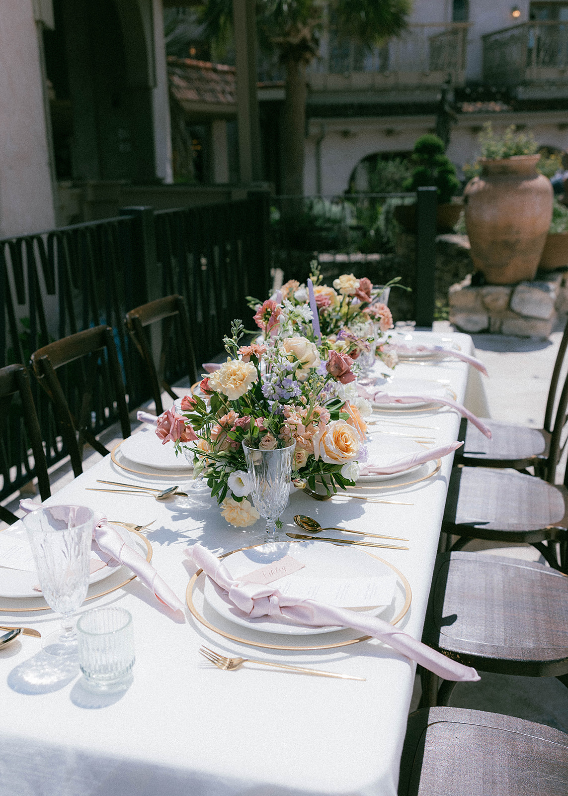 Elegant outdoor dining table with floral centerpieces, white tablecloth, and place settings. Scenic view of lush green hills under a partly cloudy sky in the background at wedding venue Villa Antonia
