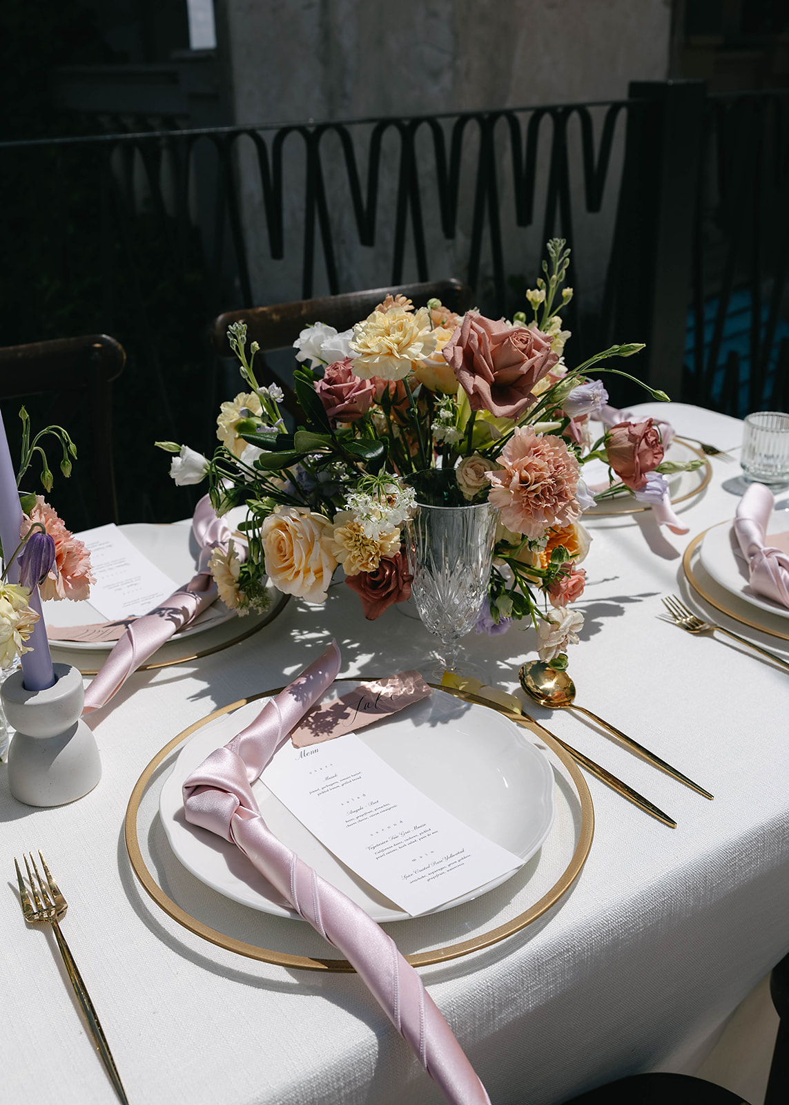 Elegant outdoor dining table with floral centerpieces, white tablecloth, and place settings. Scenic view of lush green hills under a partly cloudy sky in the background at wedding venue Villa Antonia