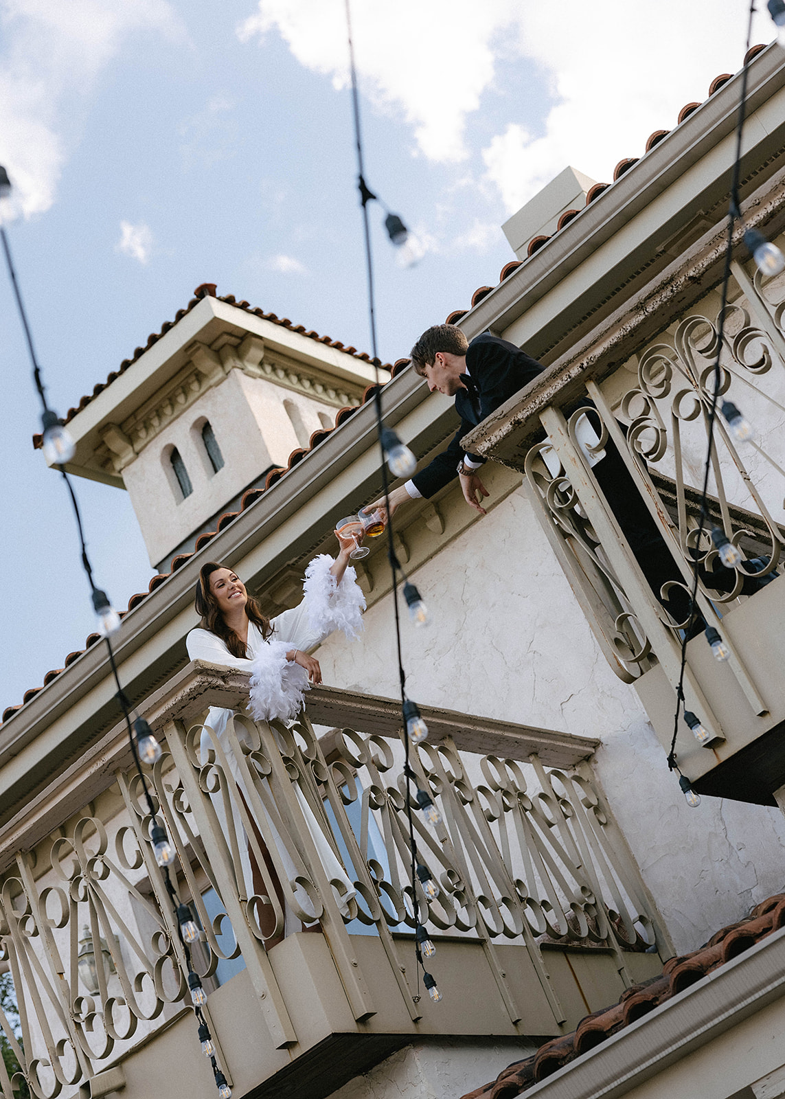 A woman in a white dress hands a flower to a man on the balcony of a two-story building at Villa Antonia