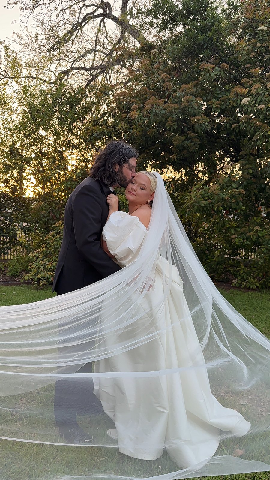 groom kisses bride on the cheek as her veil flows for a wedding at Woodbine Mansion in  Round Rock